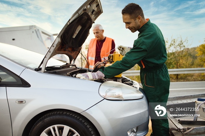 Two road assistant workers in towing service trying to start car engine with jump starter and energy station with air compressor. Roadside assistance concept.