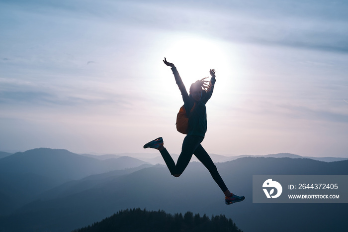 silhouette of Young woman jumping and enjoying life on mountain on sunset sky and mountains background