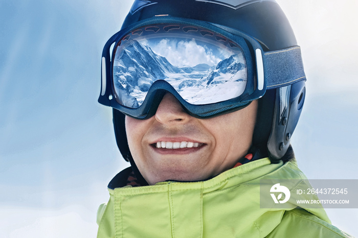 Close up of the ski goggles of a man with the reflection of snowed mountains.  A mountain range reflected in the ski mask.  Portrait of man at the ski resort on the background of mountains and sky