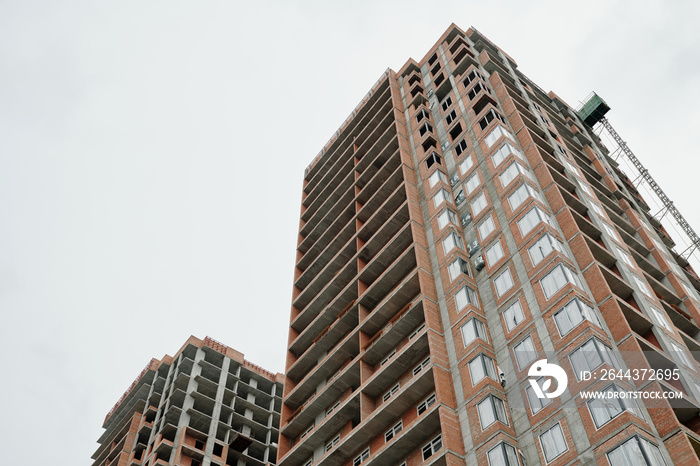 Below view of unfinished building of skyscraper or highrise condo forming block of flats against grey sky in the downtown of modern city