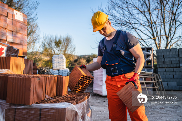 One man construction worker taking and carry or hold clay orange hollow blocks ar warehouse or construction site in sunny summer day copy space