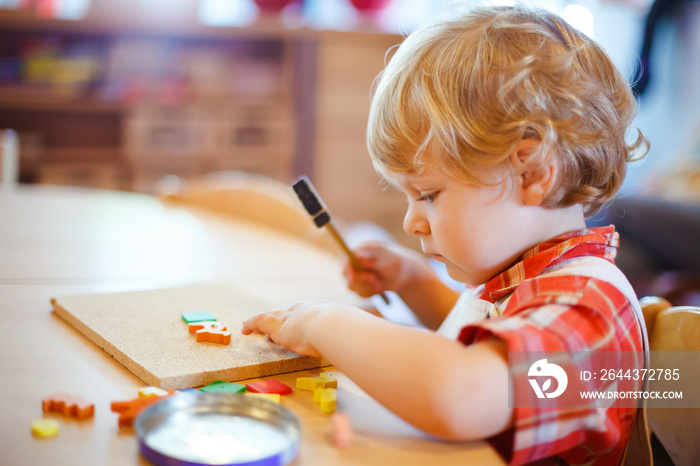 Little cute toddler boy playing with wooden puzzle hammer toys. Happy baby child playing at playschool or kindergarten. children at day care doing activity