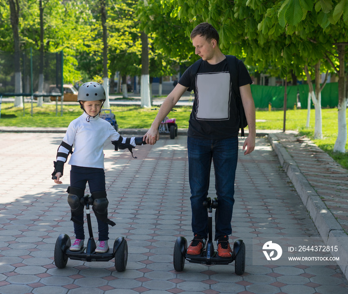 Young father teaching his daughter to ride electric mini hoverboard in park. Family concept