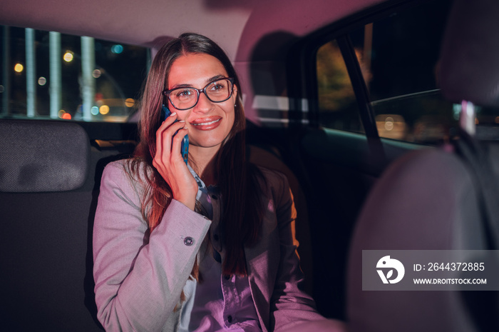 Business woman using smartphone while sitting in a backseat of a car at night