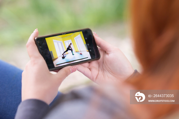 Young woman watching on the smart phone video of other woman exercise