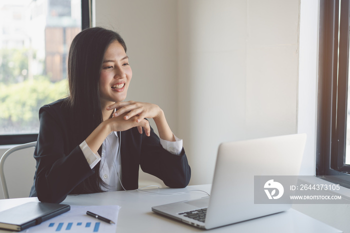 Happy young asian business woman waving hands to greeting partner during making video conference with her team.