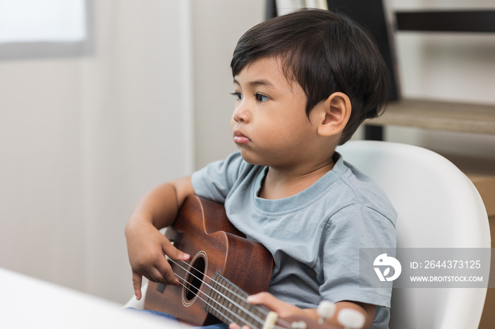 Asian little boy education from home. Developing children’s learning before entering kindergarten Practice the skills ukulele with listening to the music.