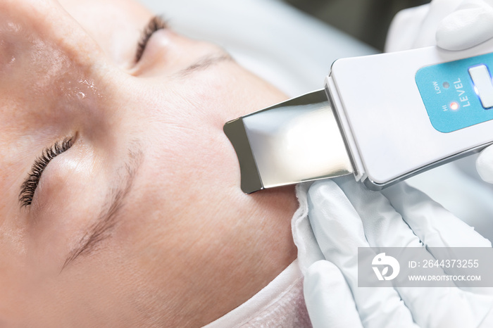 Close-up detail beautician doctor making skin care peeling cleansing procedure by ultrasonic scrubber mechanic spatula at beauty clinic salon. Specialist doing skincare treatment. Health care therapy