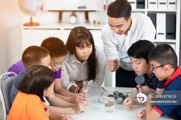 Asian teacher expanding to student in geology class with different of rock .