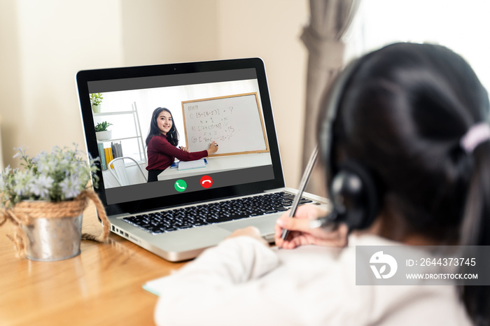 Homeschool Asian little young girl learning online class from school teacher by remote internet meeting application due to coronavirus pandemic. Female teaching math by using headphone and whiteboard.