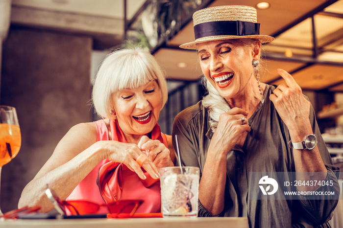 Amused good-looking old ladies being excited while drinking together