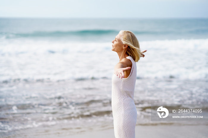 Mature woman opening her arms on the beach, spending her leisure time, enjoying her free time