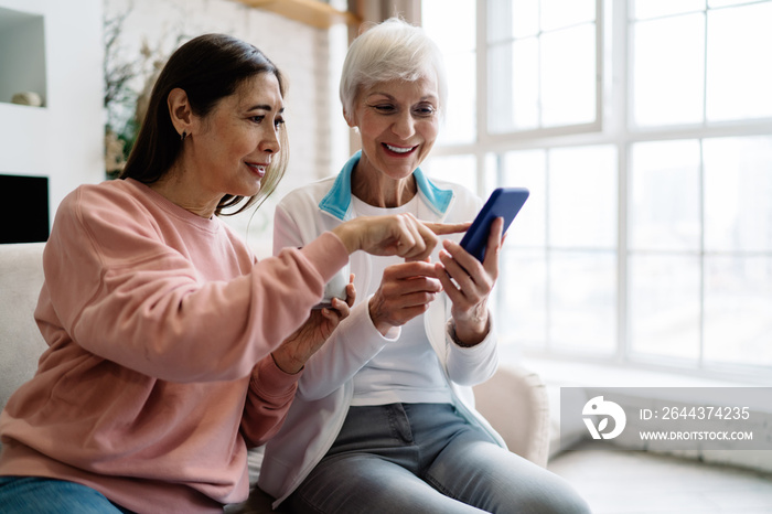 Happy senior diverse women browsing cellphone together