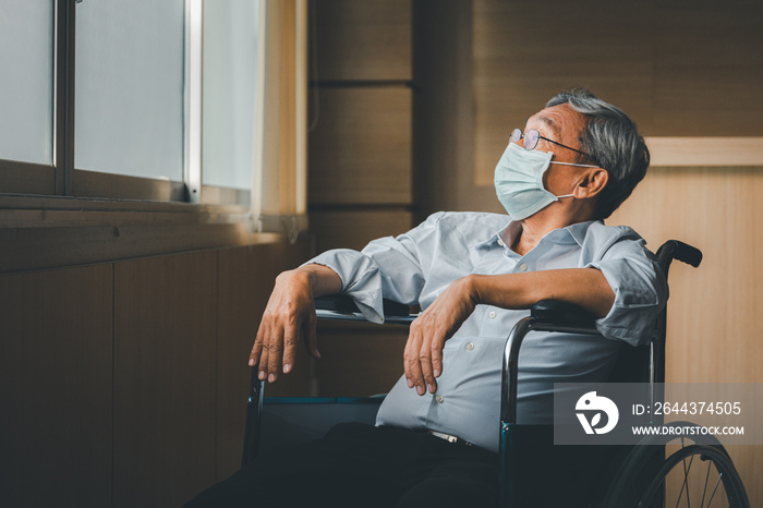 Retirement concept. Asian elderly man wear mask sitting in wheelchair while looking out the window in nursing home or hospital.