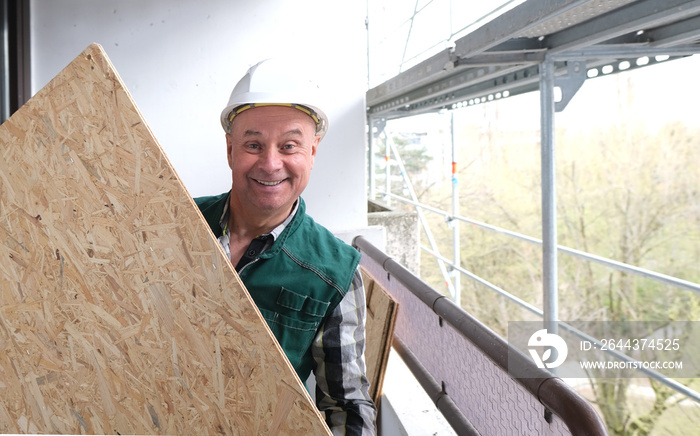 funny elderly builder with building materials in a white helmet protection and working uniform works at a construction site for the construction and repair of buildings