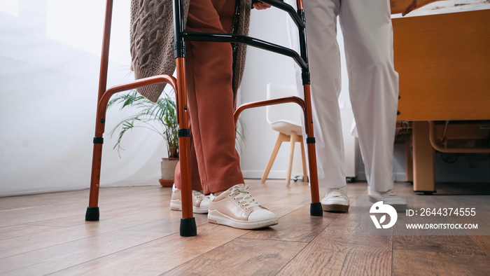 partial view of senior woman stepping with walkers near nurse