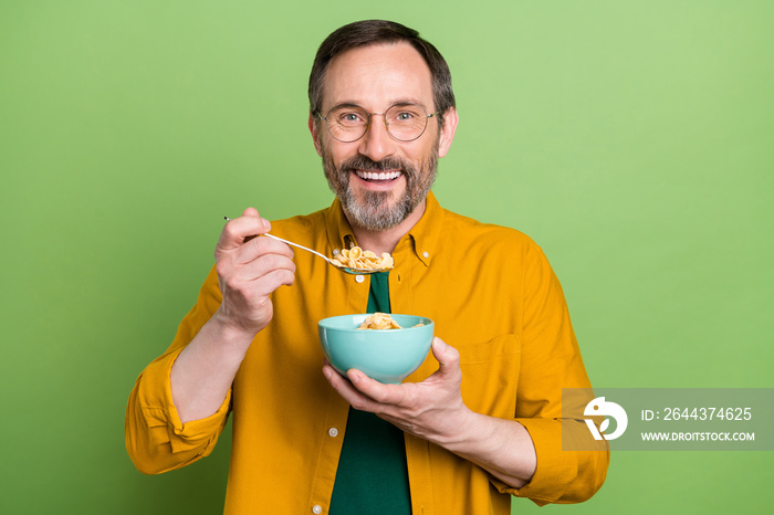 Photo of mature man happy positive smile eat cornflakes breakfast yummy isolated over green color background