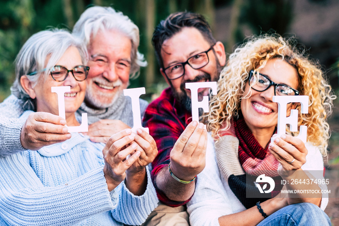 Group of mixed ages generations people smiling and showing blocks letters with  life word -  happy lifestye enjoying the outdoor leisure activity together like a family