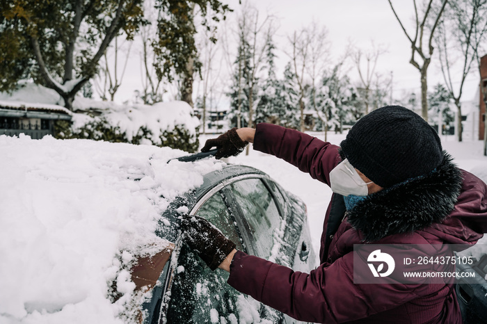 Woman digging out her car, which is covered by snow during the Storm in Spain. Concept of consequences of snowstorm