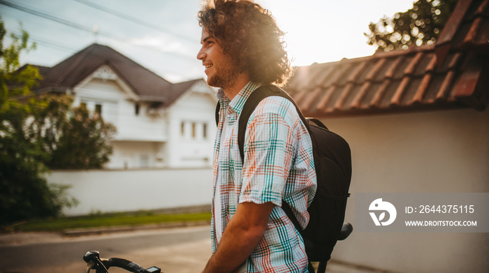 Side view portrait of happy young handsome male with curly hair with backpack, choose the bike on the city street for ecological life. Man student bicycling to the college. People, sport, lifestyle