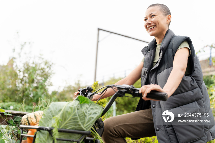 Smiling woman riding cargo electric trike loaded with homegrown vegetables