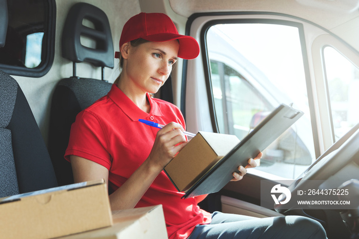 delivery woman in red uniform sitting in van and writing documents