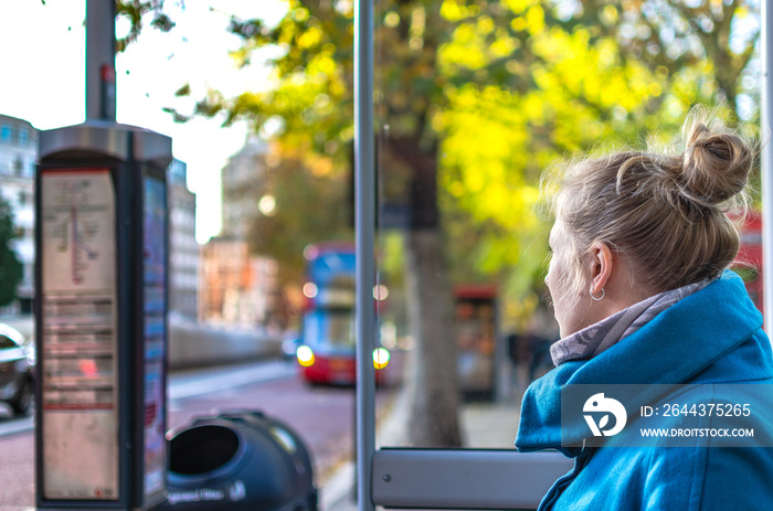 Woman in a blue coat waiting at a bus stop in London