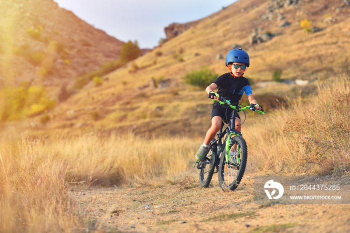 Happy kid boy of 7 years having fun in autumn park with a bicycle on beautiful fall day. Active child wearing bike helmet