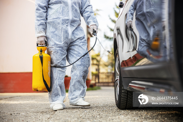 Man in protective suit with mask disinfecting car tires, prevent infection of Covid-19 virus coronavirus,contamination of germs or bacteria. Infection prevention and control of