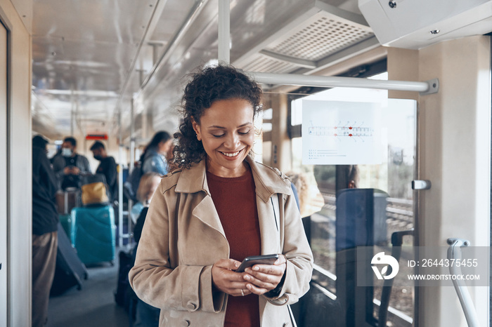 Beautiful mature woman using smart phone and smiling while traveling by train