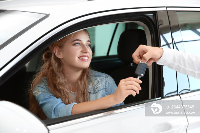 Young woman receiving key while sitting on driver’s seat of car