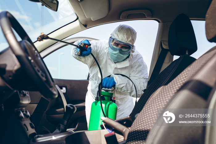 Man in protective suit with mask disinfecting inside car.