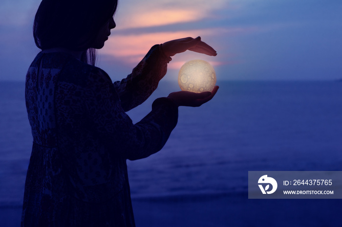 Beautiful attractive girl on a night beach with sand and stars holds the moon in her hands