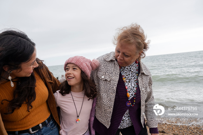 Grandmother, mother and daughter walking on beach on cloudy day