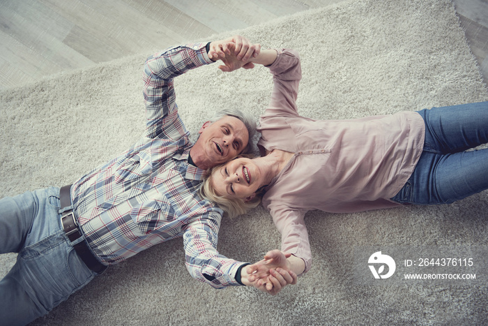 Top view portrait of retired male and female people lying on carpet and holding their hands. They are delighted