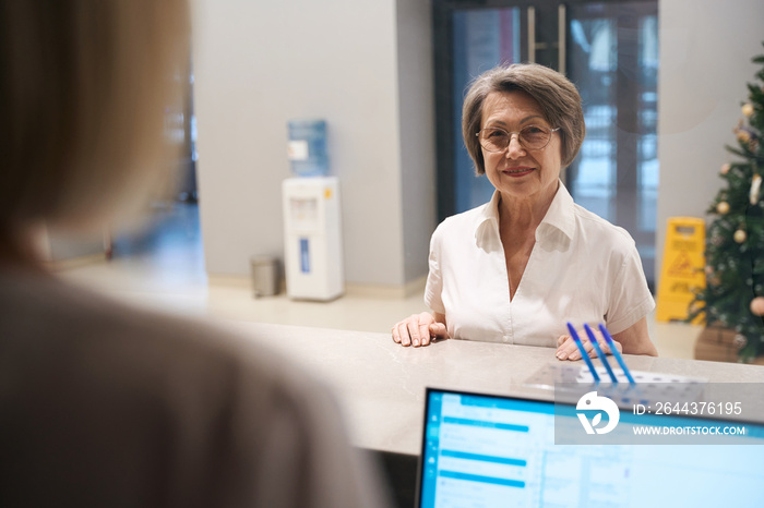 Elderly woman stands at the reception desk in the clinic