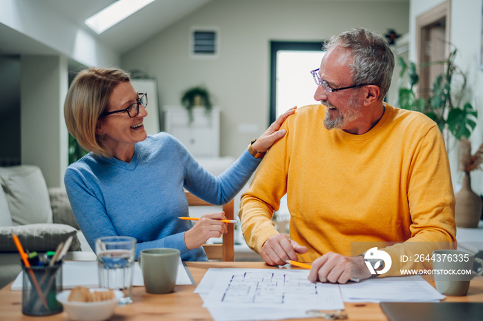 Senior couple sitting at table and looking into blueprints of their new home