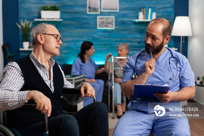 Support assistant man worker writing medication treatment on clipboard discussing with disabled senior male patient during assistance healthcare service. Social services nursing at home