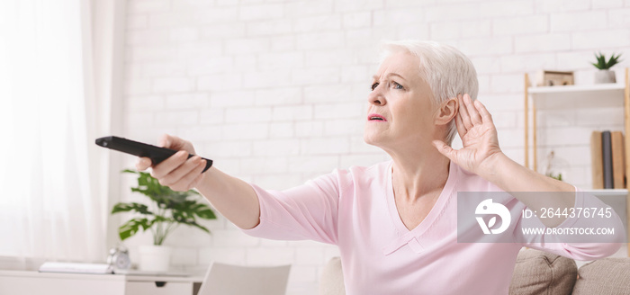 Elderly woman rising tv set volume with remote control