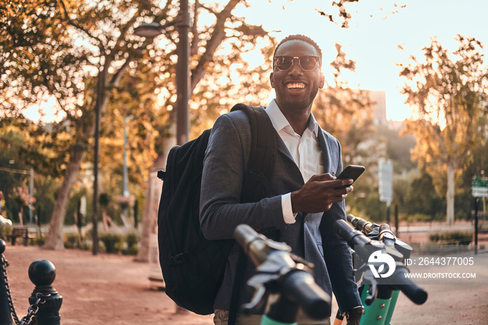 Attractive american tourist in sunglasses is paying for electrical scooter using his mobile phone.