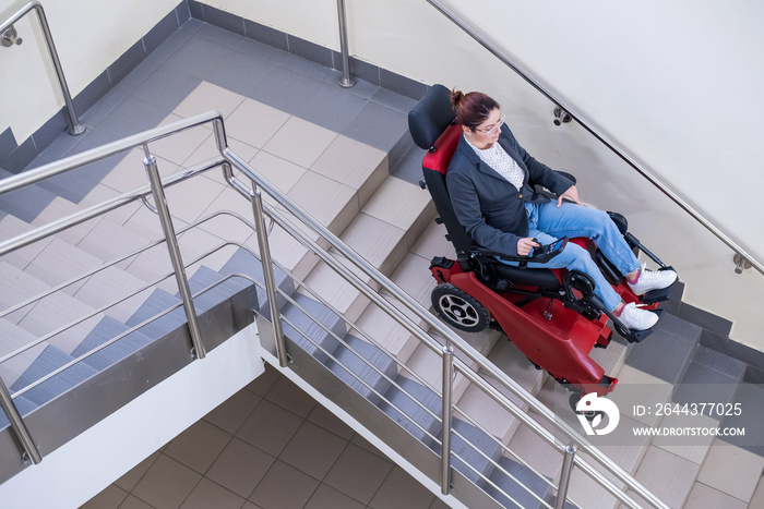 Caucasian woman in wheelchair with electric caterpillar going down stairs.