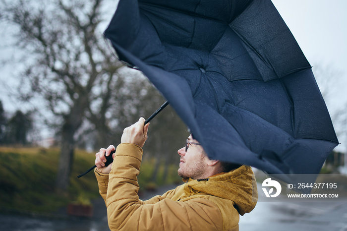 Man holding broken umbrella in strong wind during gloomy rainy day. Themes weather and meteorogy. .