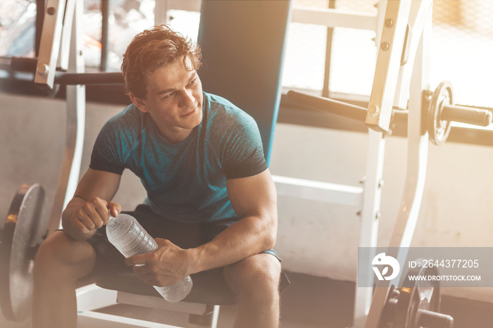 Portait of young man going to exercise in gym. He is looking aside and holding a bottle of water. Horizontal shot