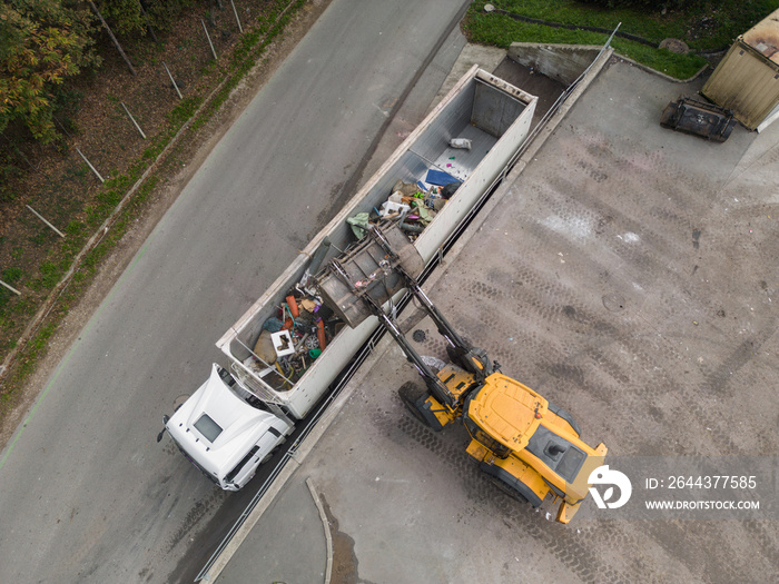 Waste loading operation, loader dumping trash in a truck on a site for the disposal of waste materials, drone shot.