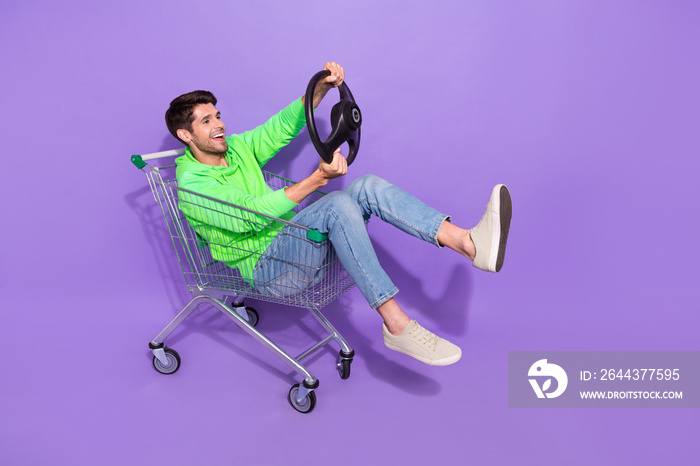 Full length photo of pretty funky man wear green hoodie supermarket tray rider driving auto empty space isolated purple color background