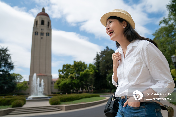 cheerful asian Japanese lady tourist looking at famous landmark hoover tower at distance while visiting school university in California usa on a sunny day in spring