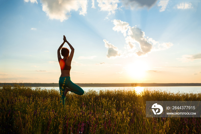 Silhouette of sportive girl practicing yoga in field at sunrise.