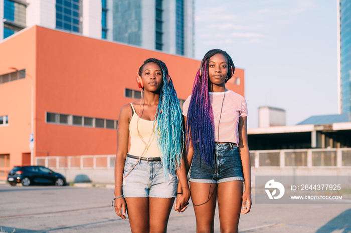 Portrait of sisters listening to music while standing outdoors