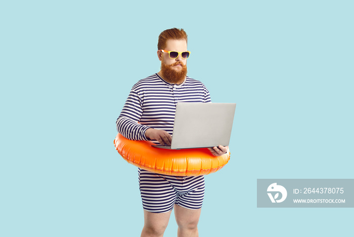 Funny man finds time for business during summer holiday at seaside. Serious chubby entrepreneur working on computer while on vacation. Busy plus size guy in striped swimsuit using his laptop at beach