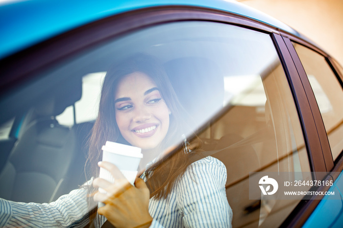 Young woman drinking coffee while driving her car. Drinking morning coffee while driving to work. Portrait of a young and cheerful woman with coffee cup driving luxury car in the city